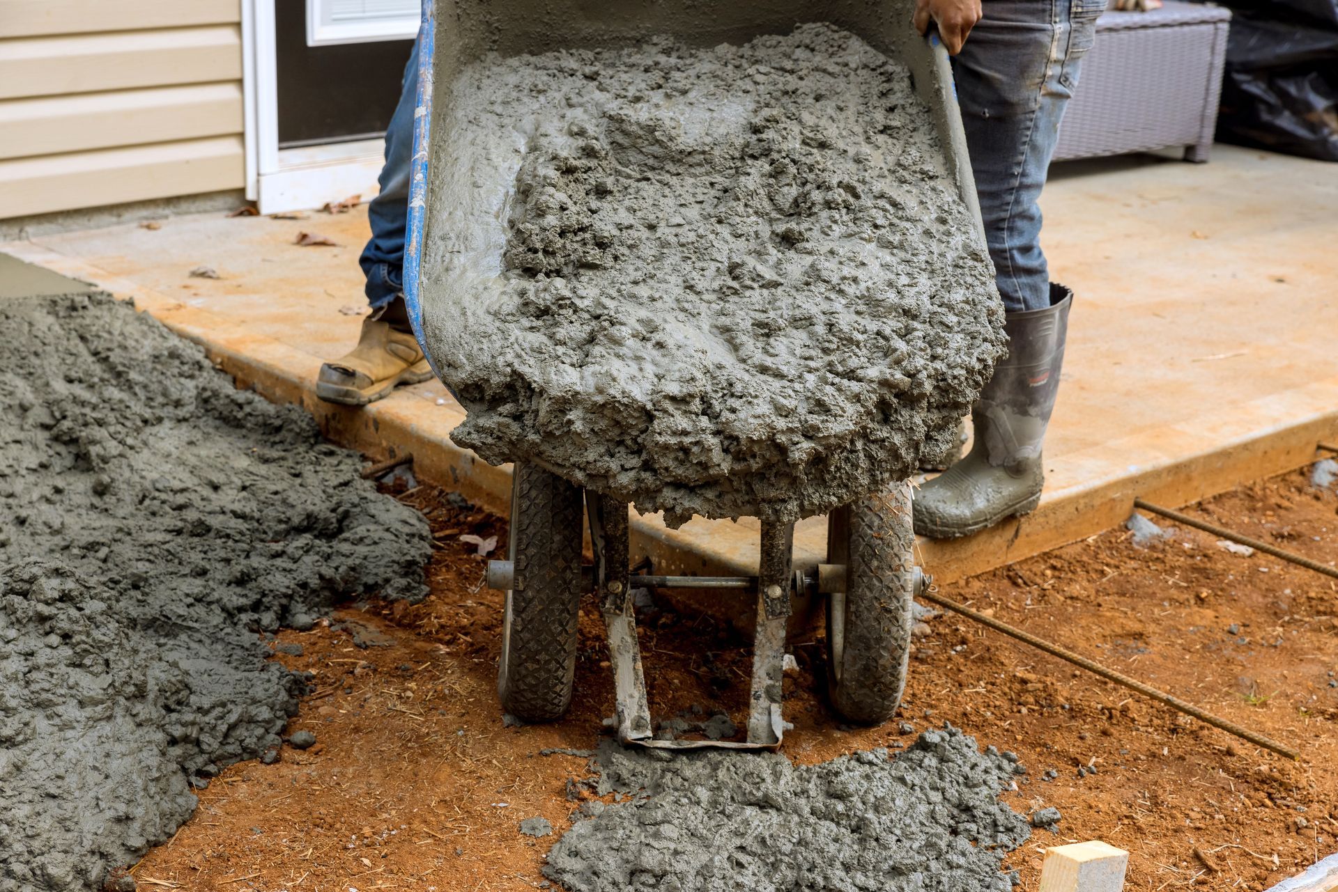 A person is pouring concrete into a wheelbarrow.