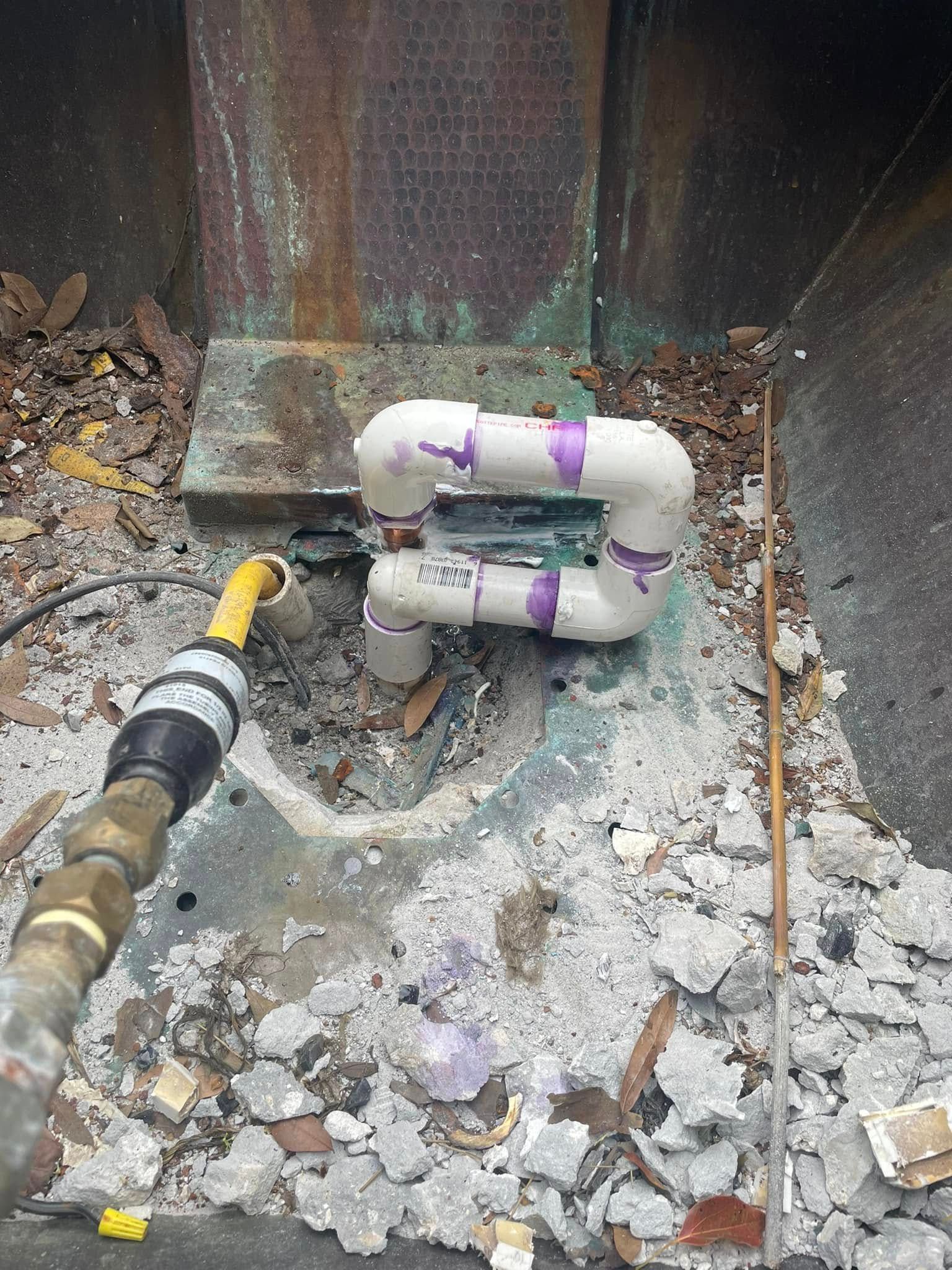 White PVC pipe assembly with purple primer joints emerging from a concrete floor next to a yellow hose nozzle.