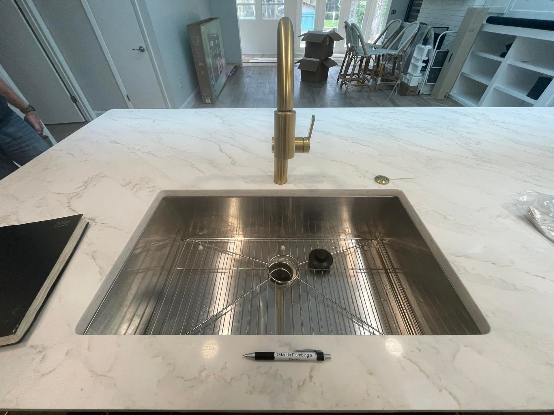 Stainless steel kitchen sink in a white countertop with gold faucet.