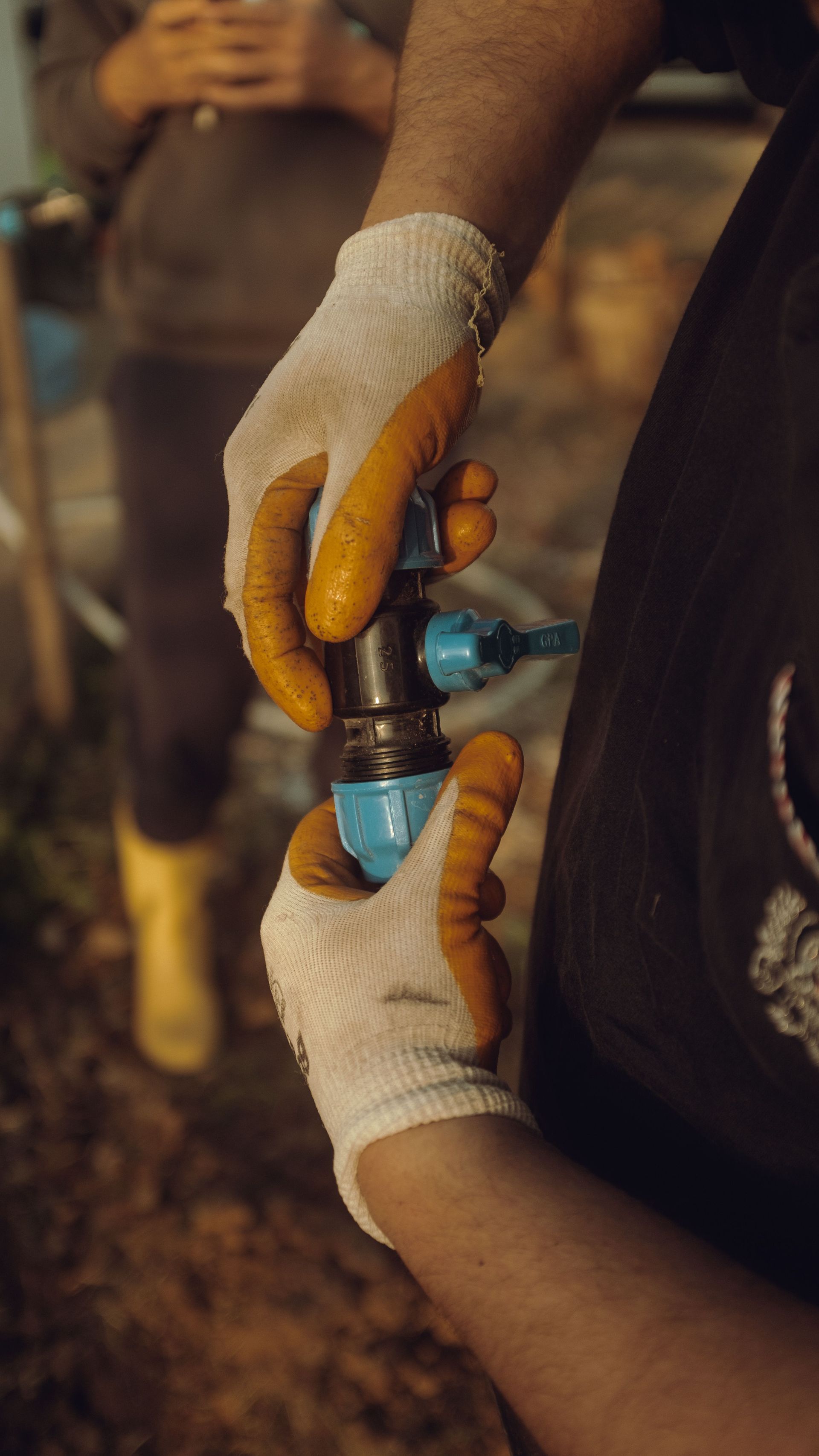 Gloved hands twisting a blue water valve on a pipe outdoors