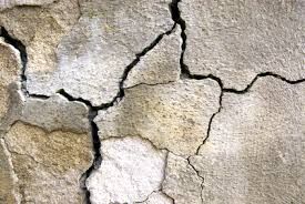 Close-up of a weathered, cracked wall with irregular lines and varying shades of gray and beige.