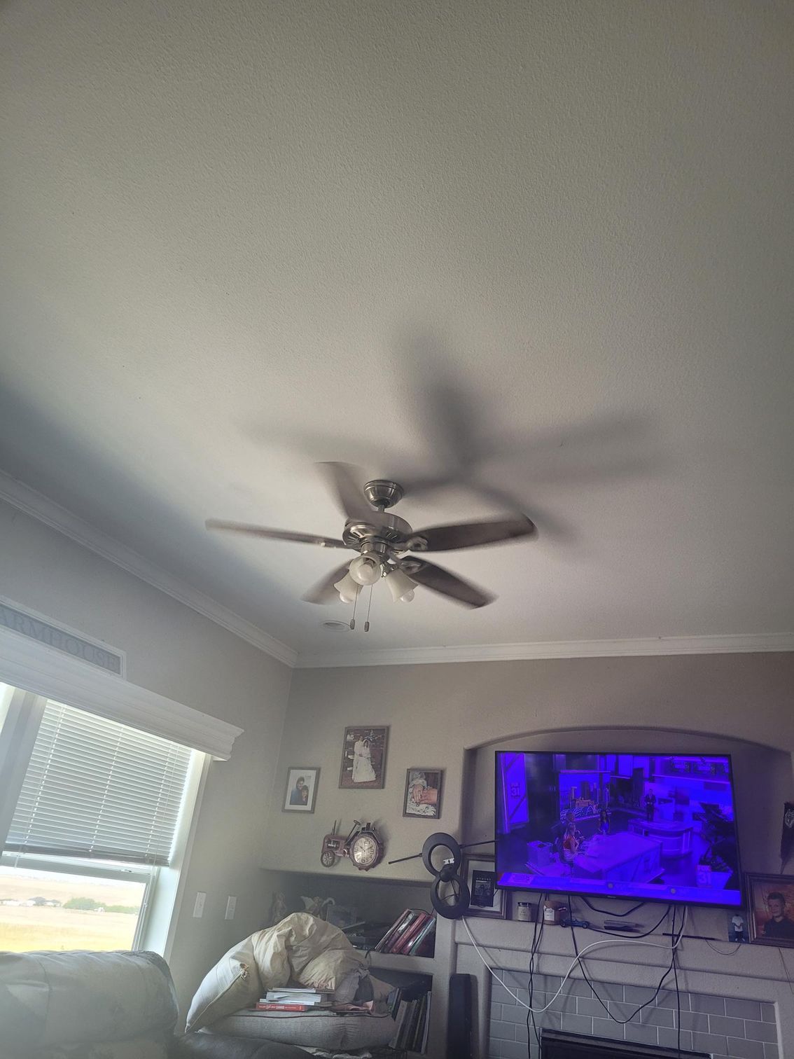 Ceiling fan casts a shadow in a room with a TV and window.