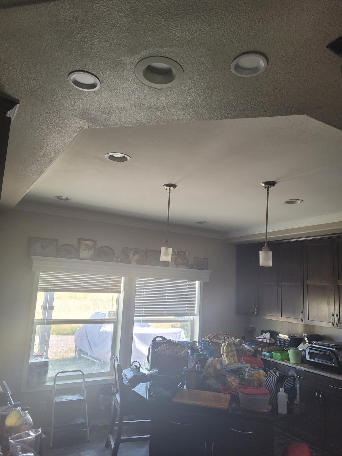 Kitchen ceiling with recessed lights and pendant lights over a cluttered island.