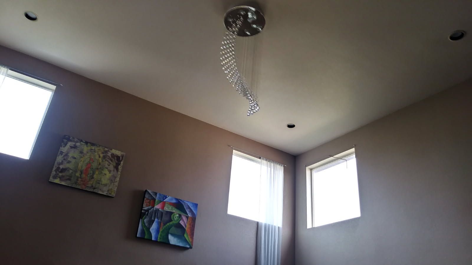 Brown-walled room with chandelier, artwork, and small windows letting in sunlight.