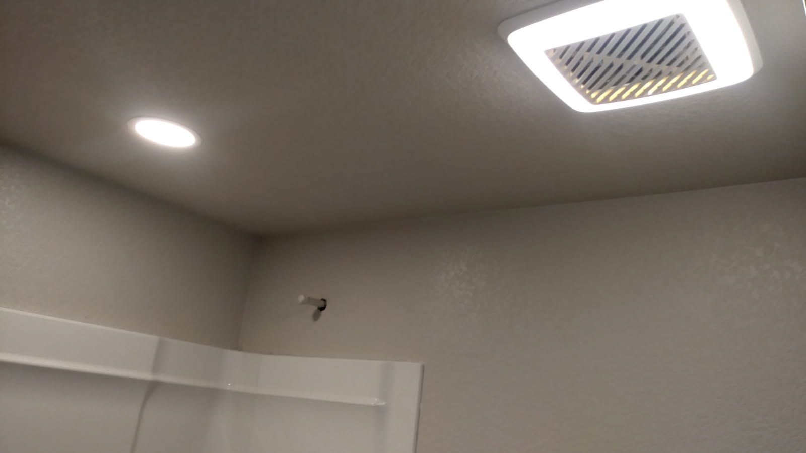 Corner of a bathroom ceiling with recessed lighting and a vent fan. The walls are painted gray.