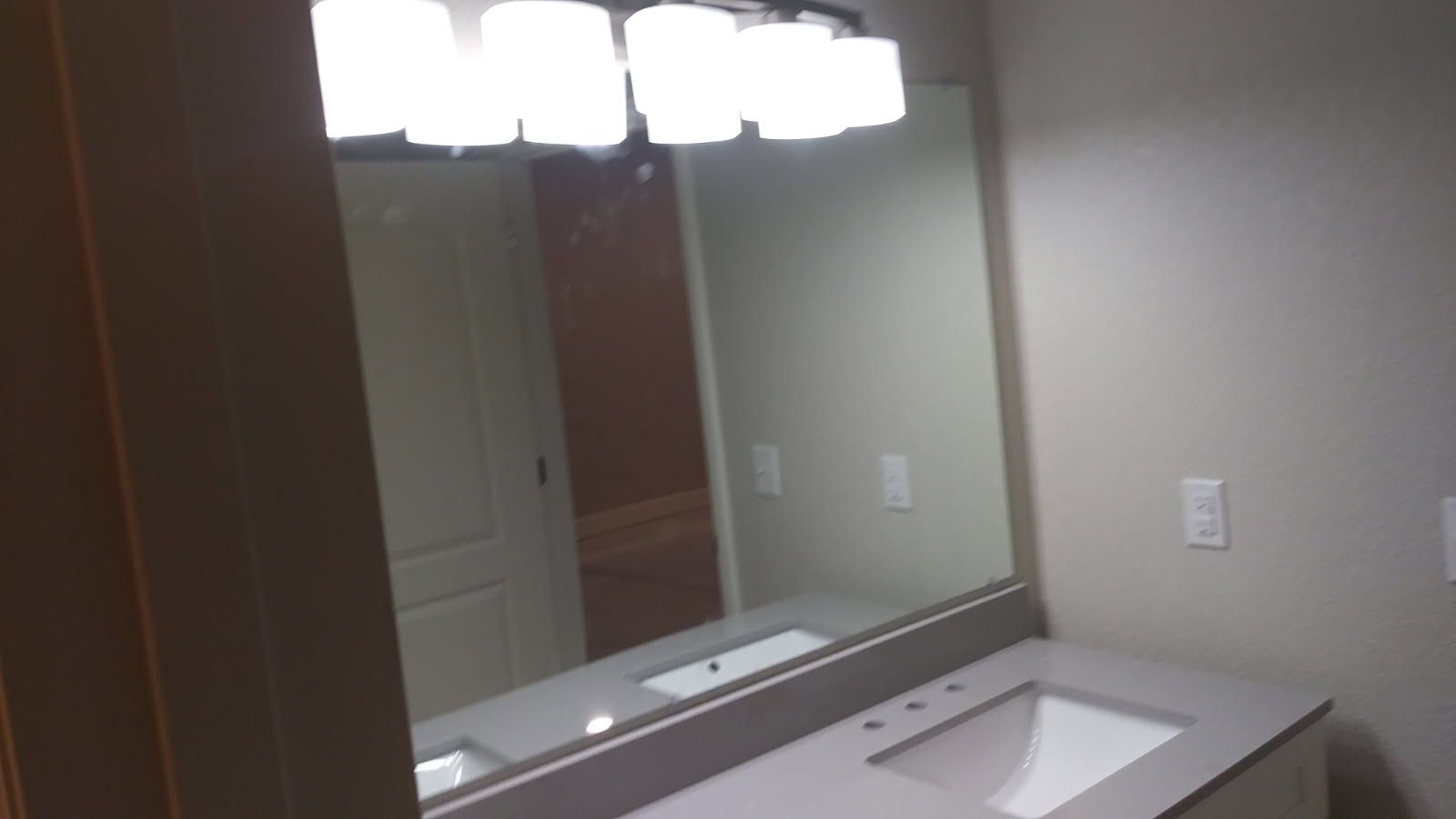 Bathroom with large mirror over a sink and vanity, and a light fixture above the mirror.