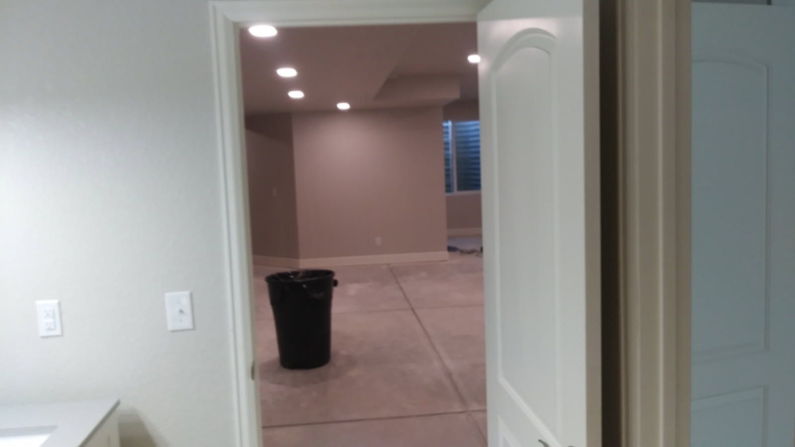 Doorway into a room with a trash can, recessed lighting, and unfinished flooring.
