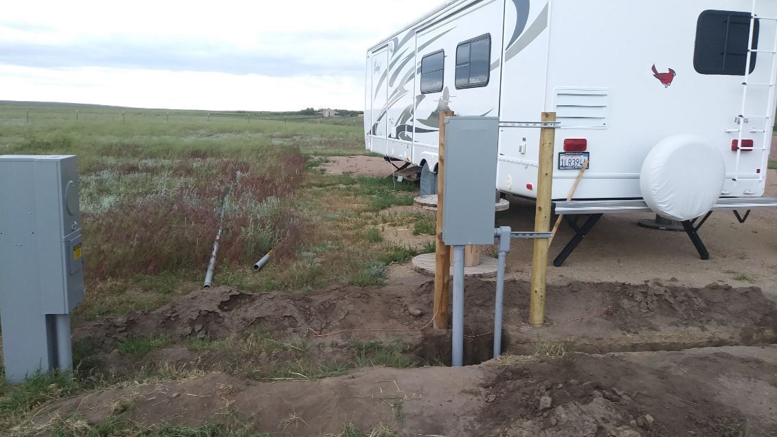 RV parked near electrical hookup with gray utility boxes, outdoors.
