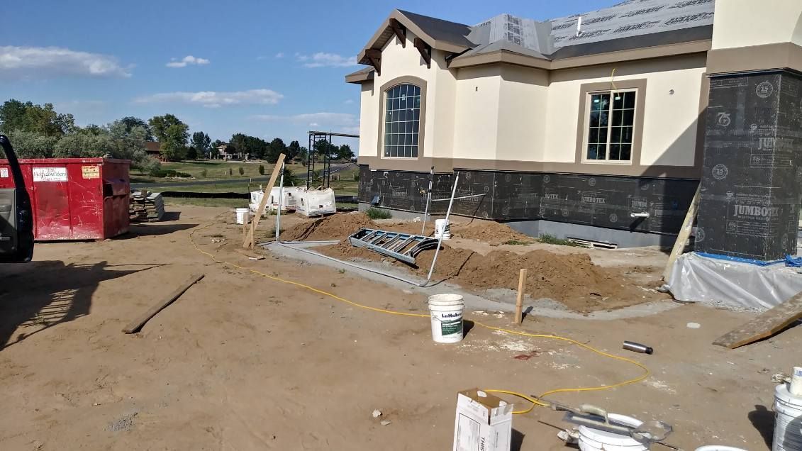 Construction site of a beige house with black underlayment; dirt and debris surround.