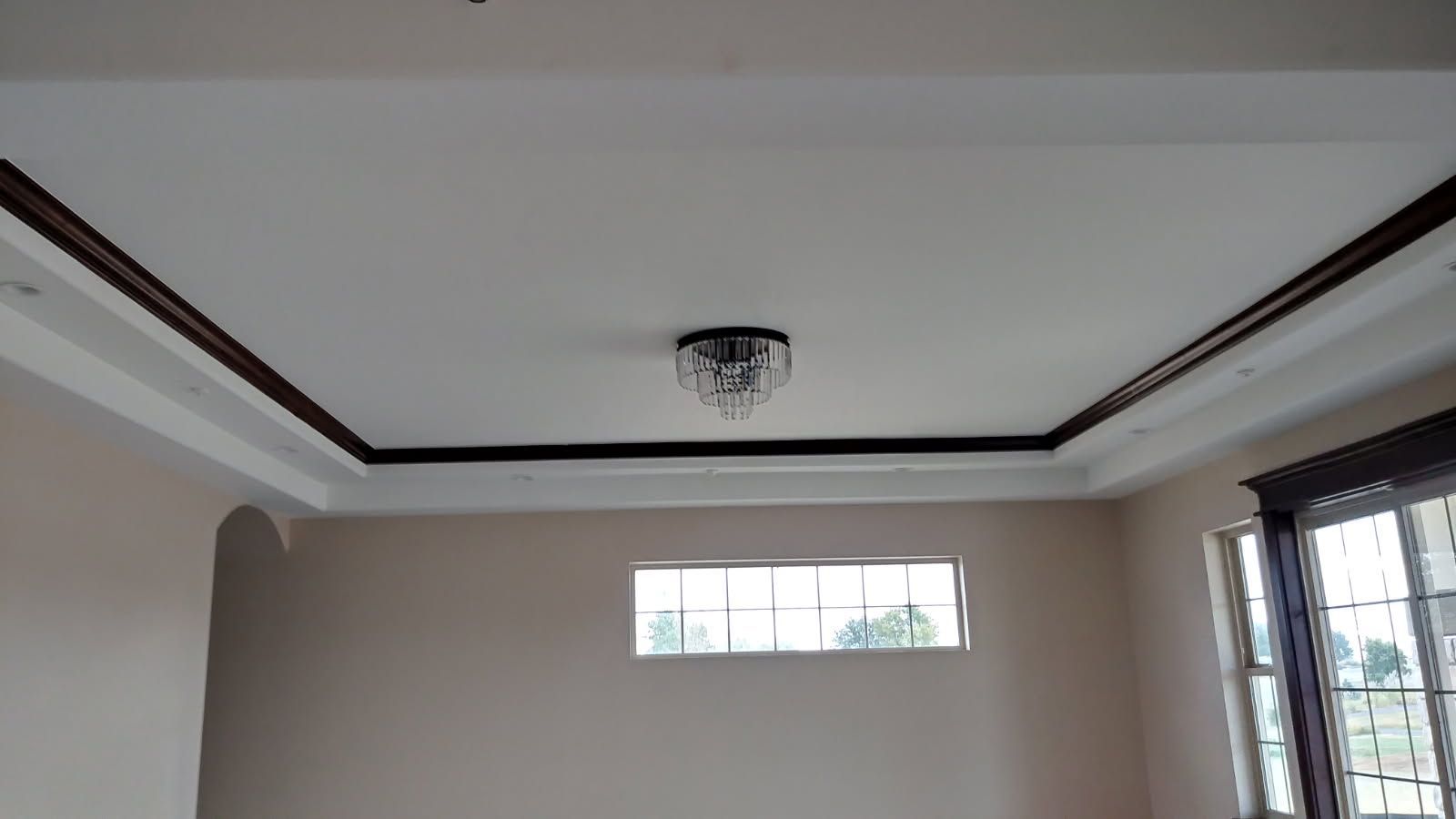 Interior view of a room with a coffered ceiling, chandelier, and windows. Neutral colors, natural light.