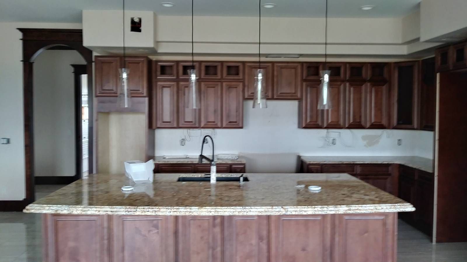 Kitchen with brown cabinets, granite island, and hanging lights; under construction.