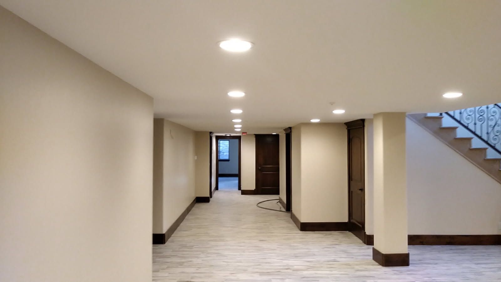 Hallway with recessed lighting, beige walls, dark wood doors and trim, staircase on right.