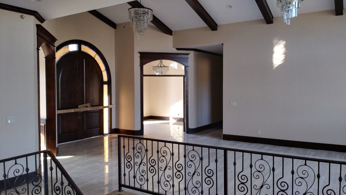 Interior view of a home with a wrought-iron railing, large wooden door, and chandelier. Light beige walls.