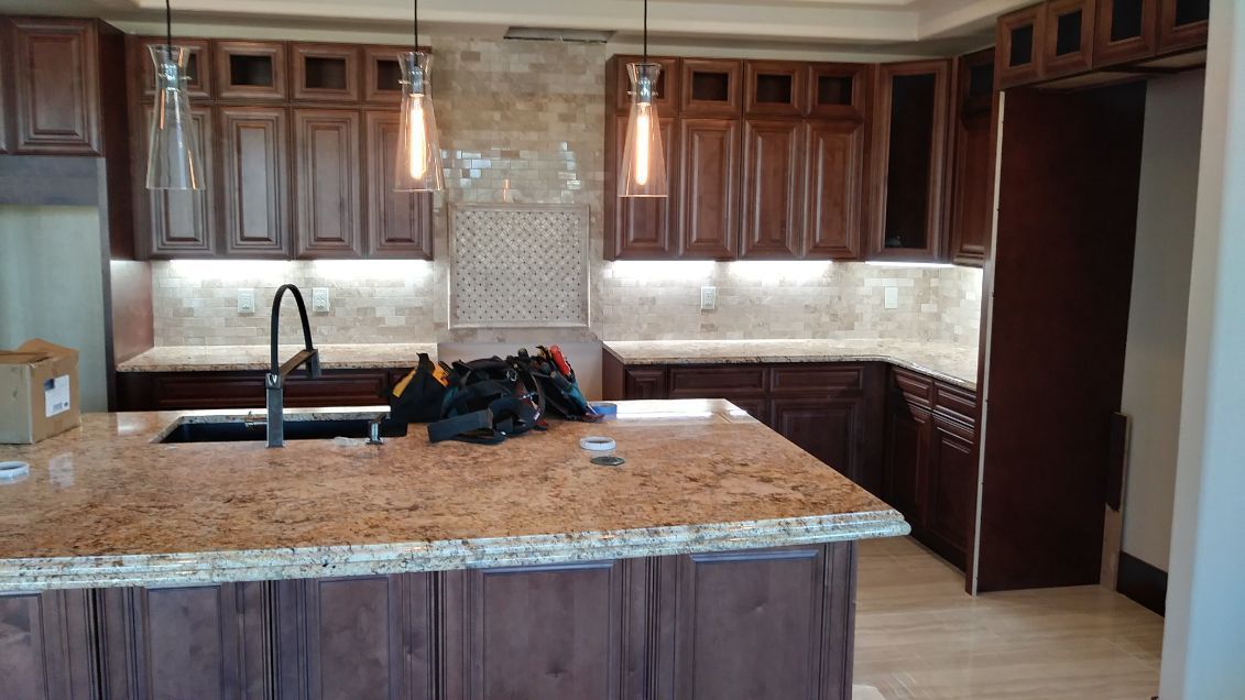 Kitchen with brown cabinets, granite countertops, island, and pendant lights.