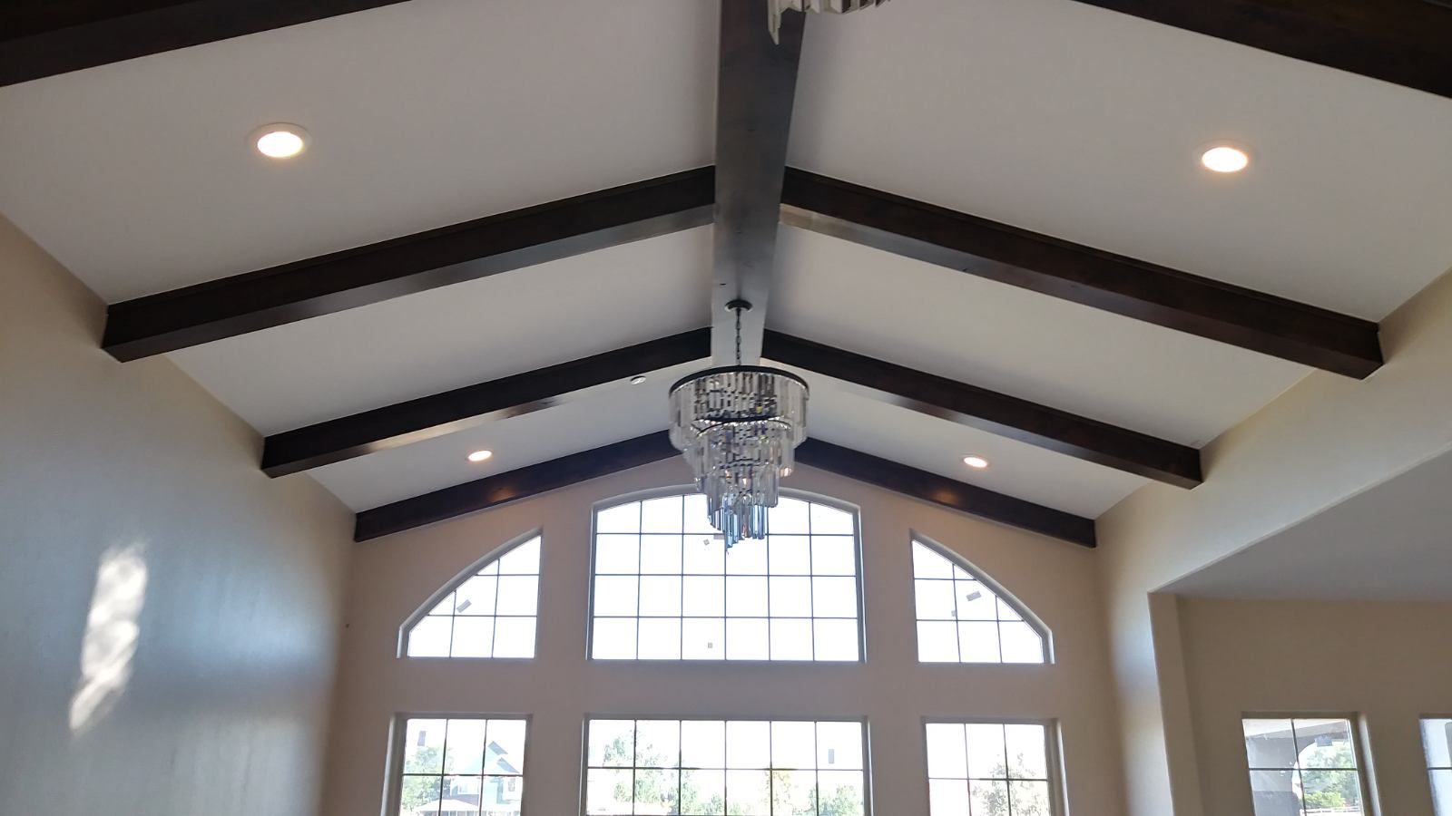 Vaulted ceiling with dark brown beams, recessed lights, and a crystal chandelier over arched windows.
