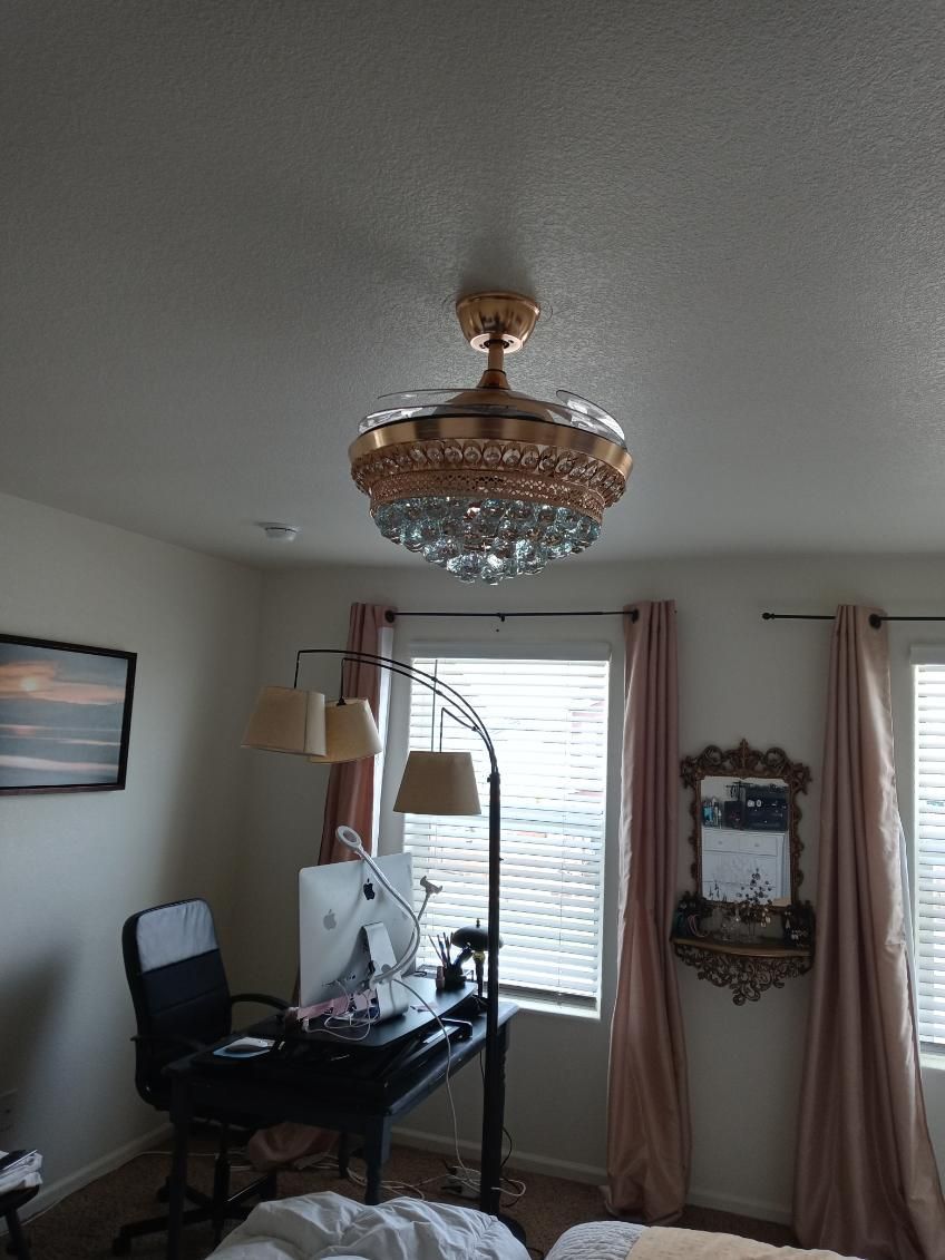 Bedroom with a gold chandelier ceiling fan, desk, and pink curtains.