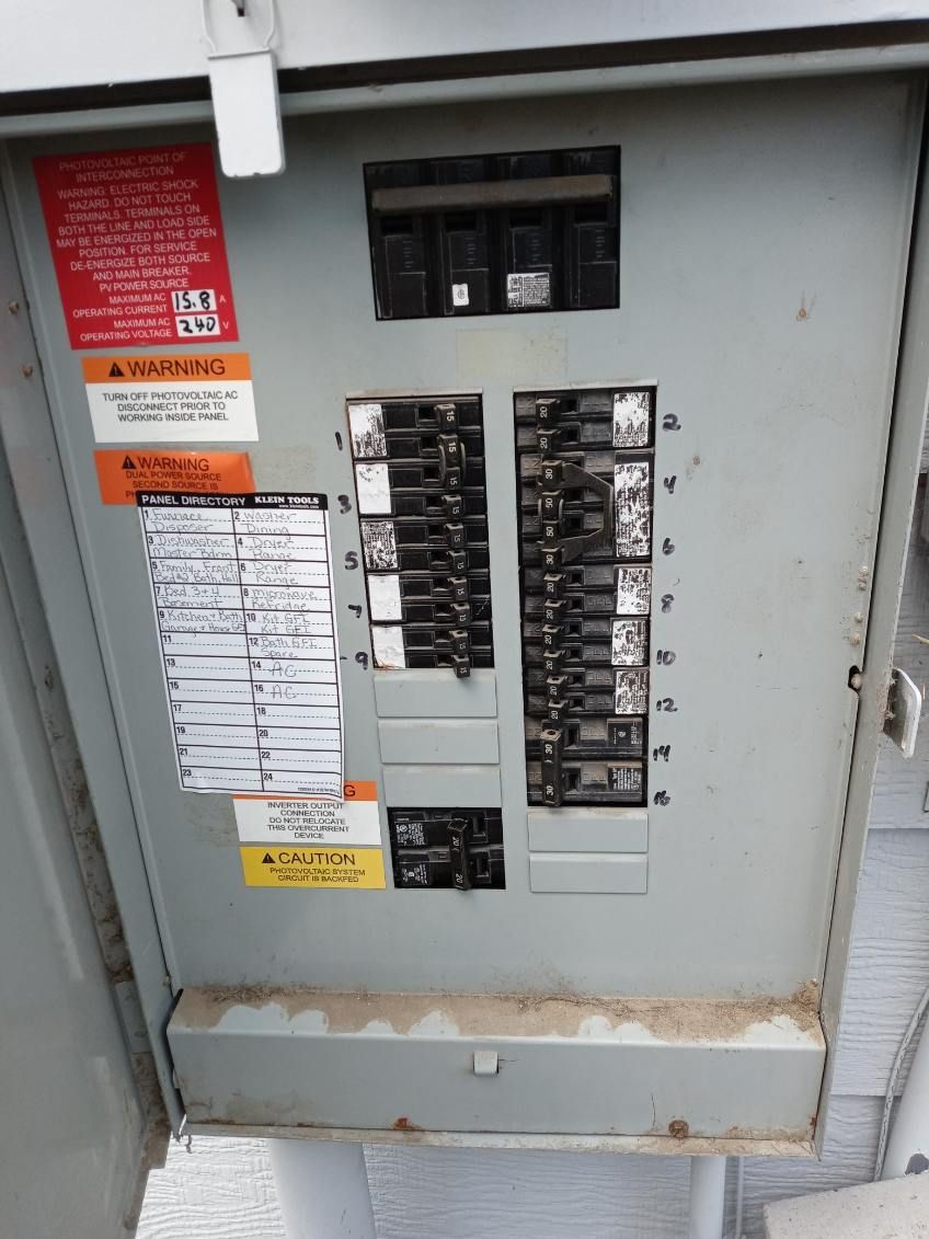 Open gray electrical panel with multiple circuit breakers and warning labels.