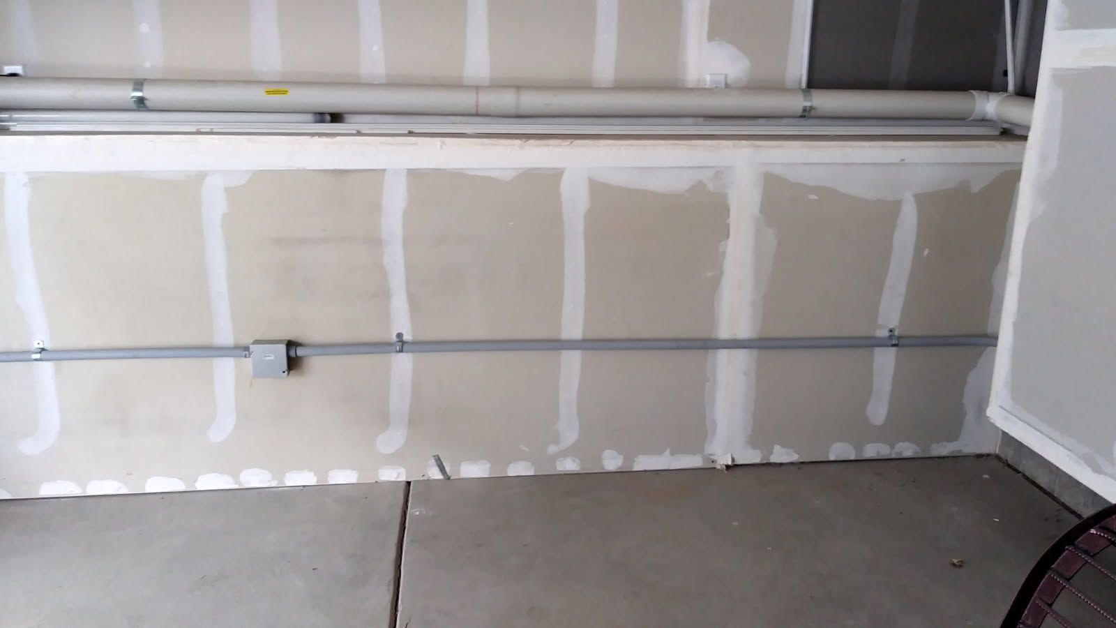 Unfinished drywall wall with electrical conduit and concrete floor in a garage.