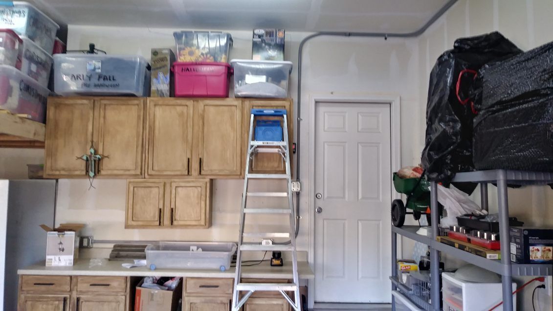 Garage interior with cabinets, storage bins, a ladder, and a door.