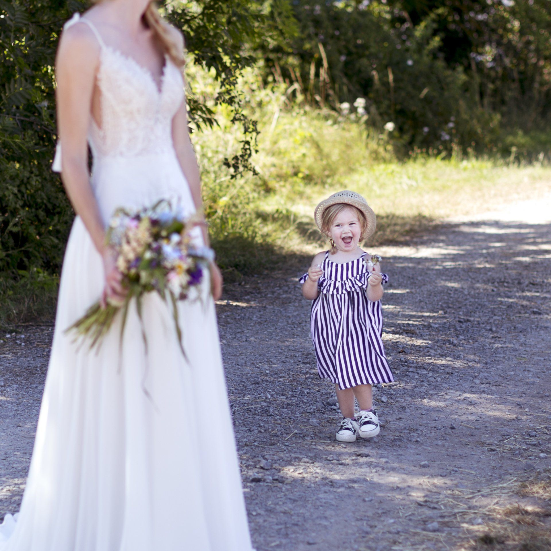 Ein kleines Mädchen steht neben einer Frau im Brautkleid, die einen Blumenstrauß hält.