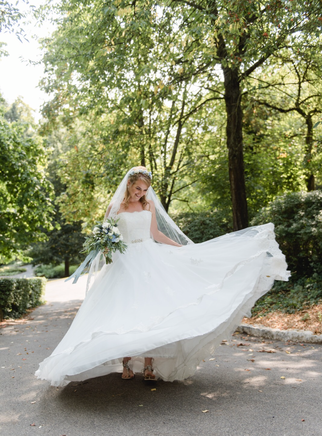 Eine Braut im Brautkleid steht auf einer Straße im Wald.