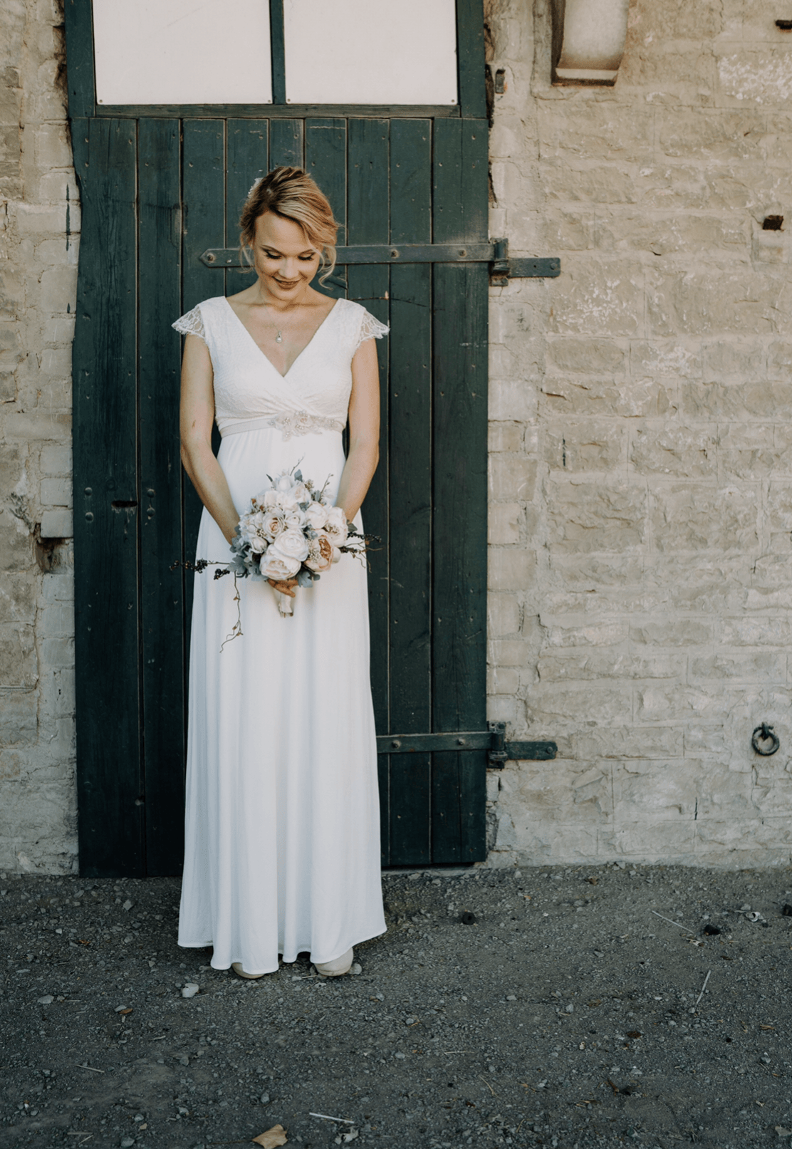 Eine Frau in einem weißen Kleid steht mit einem Blumenstrauß in der Hand vor einer Tür.