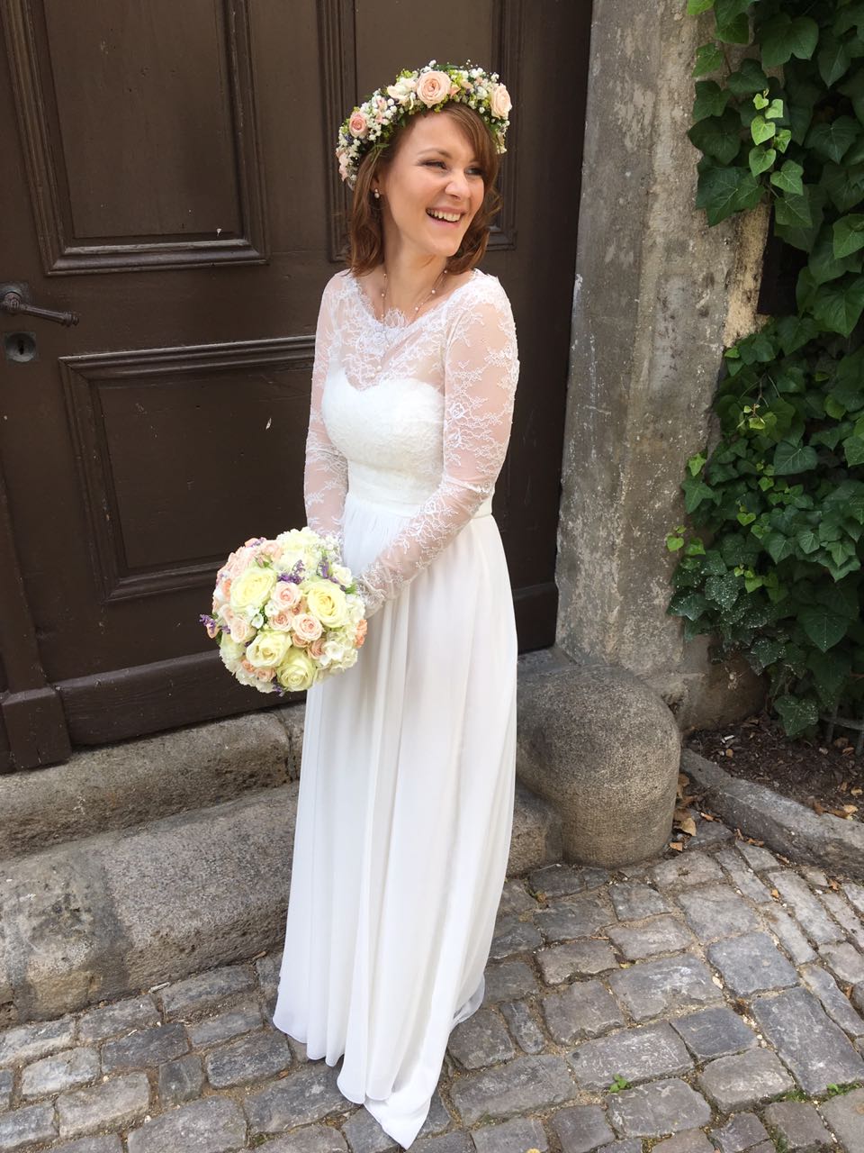 Die Braut trägt einen Blumenkranz und hält einen Blumenstrauß in der Hand.