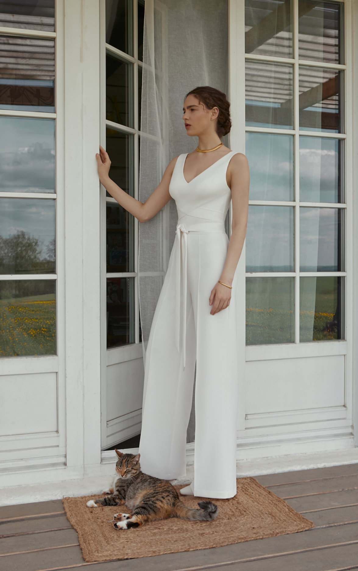 Eine Frau in einem weißen Overall steht neben einer Katze vor einer Tür.