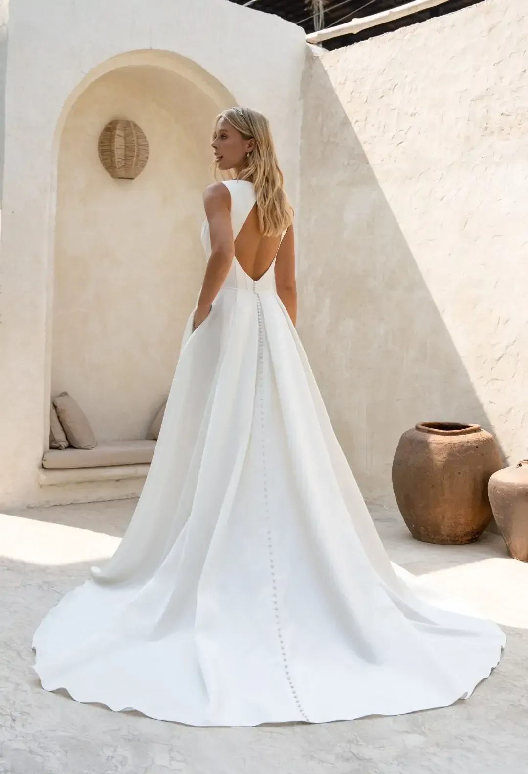 Eine Frau in einem weißen Brautkleid steht vor einer weißen Wand.