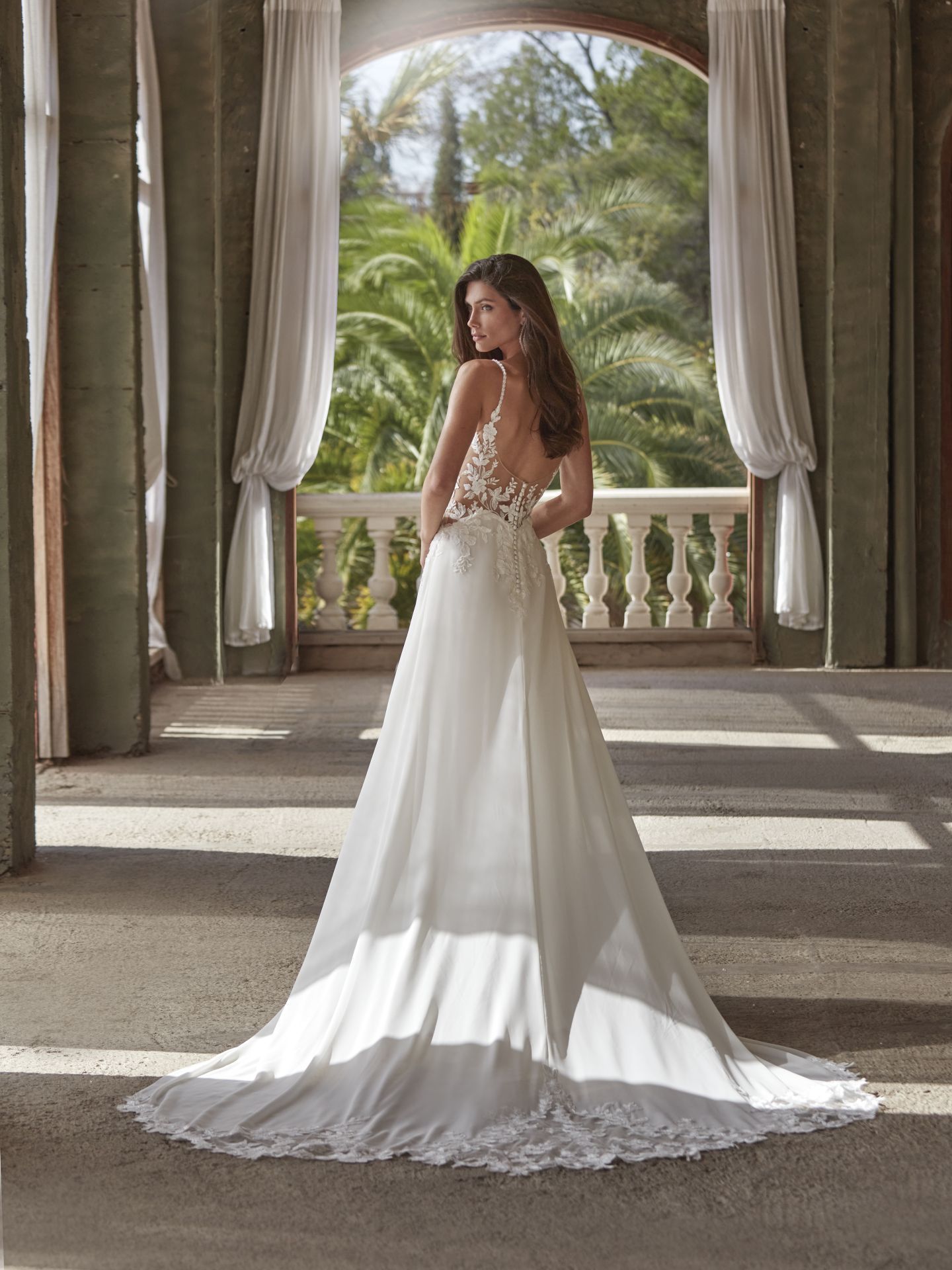 Eine Frau in einem weißen Brautkleid steht vor einem Fenster.