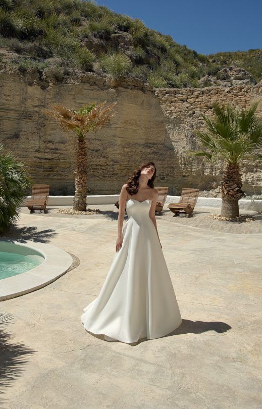 Eine Frau in einem weißen Brautkleid steht neben einem Pool.