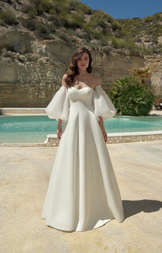 Eine Frau in einem weißen Brautkleid steht neben einem Pool.