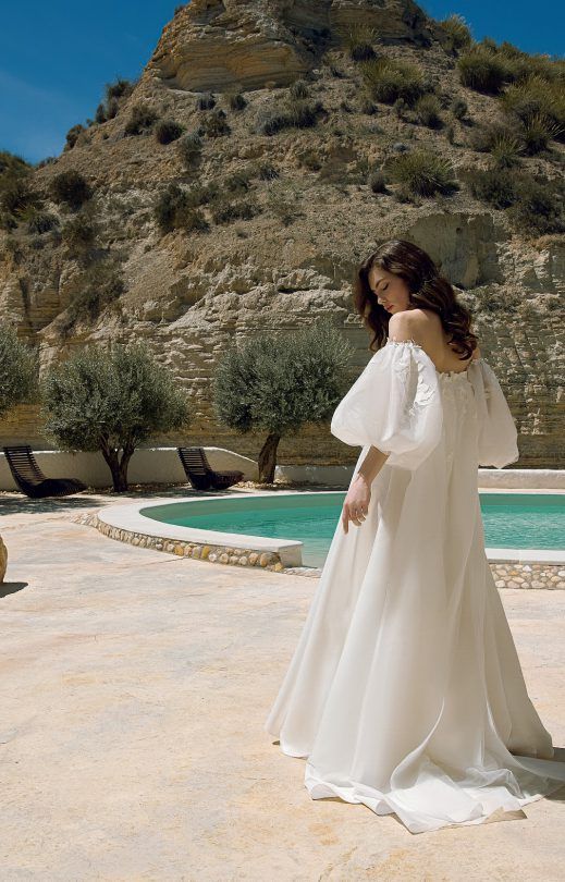 Eine Frau in einem weißen Brautkleid steht neben einem Pool.