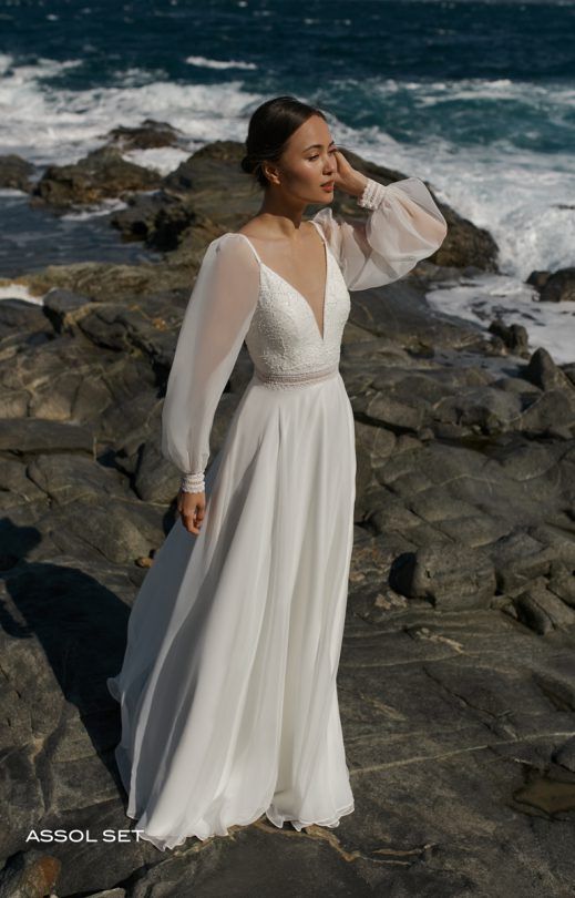 Eine Frau in einem weißen Kleid steht auf einem Felsen in der Nähe des Ozeans.