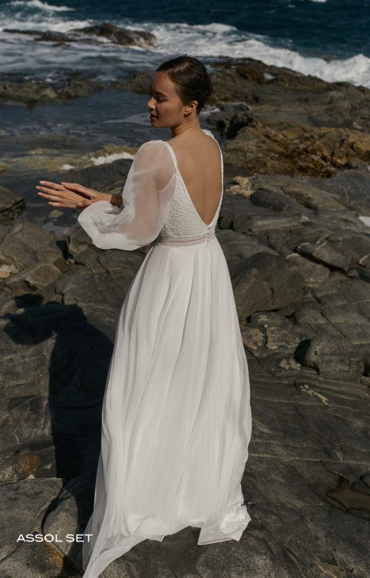 Eine Frau in einem weißen Brautkleid steht an einem steinigen Strand.