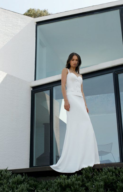 Eine Frau in einem weißen Kleid steht vor einem weißen Gebäude.