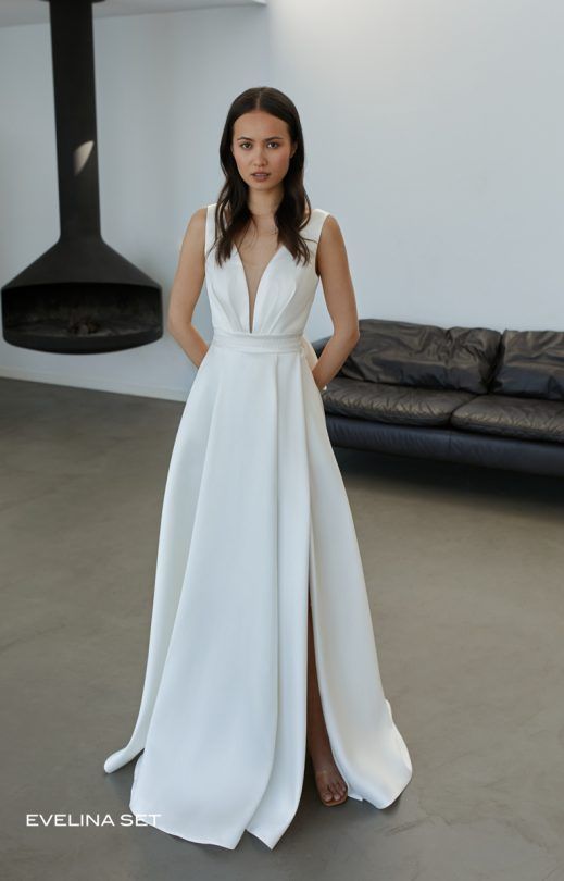 Eine Frau in einem weißen Kleid steht in einem Wohnzimmer neben einem Sofa.