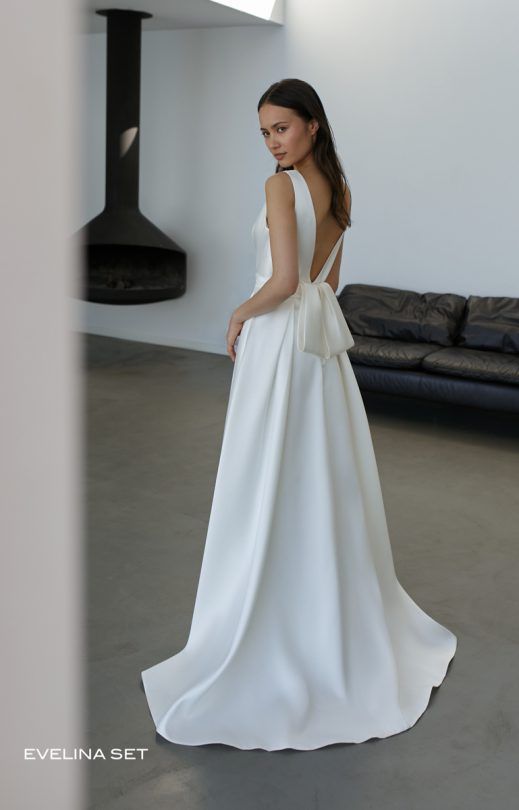 Eine Frau in einem weißen Brautkleid steht in einem Wohnzimmer.