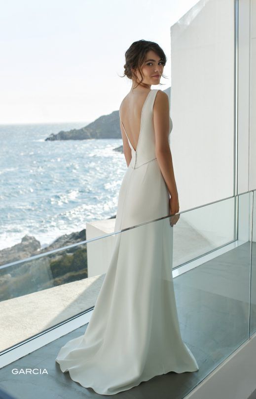 Eine Frau in einem weißen Brautkleid steht vor einem Fenster mit Blick auf den Ozean.