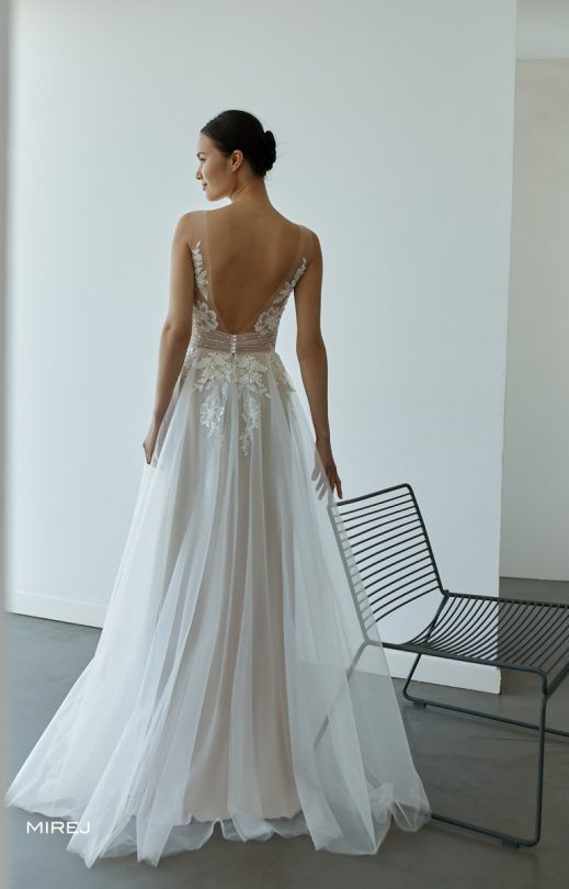 Eine Frau in einem weißen Brautkleid steht neben einem Stuhl.