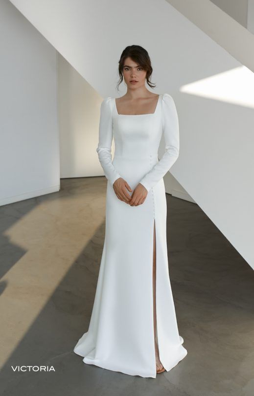 Eine Frau trägt ein weißes Kleid mit langen Ärmeln und einem hohen Schlitz.