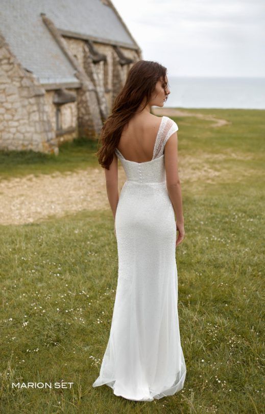 Eine Frau in einem weißen Brautkleid steht auf einem Feld vor einem Gebäude.