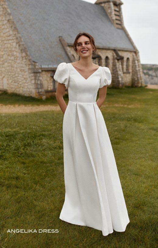Eine Frau in einem weißen Kleid steht vor einer Kirche.