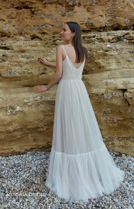 Eine Frau in einem weißen Kleid steht neben einer Felswand.