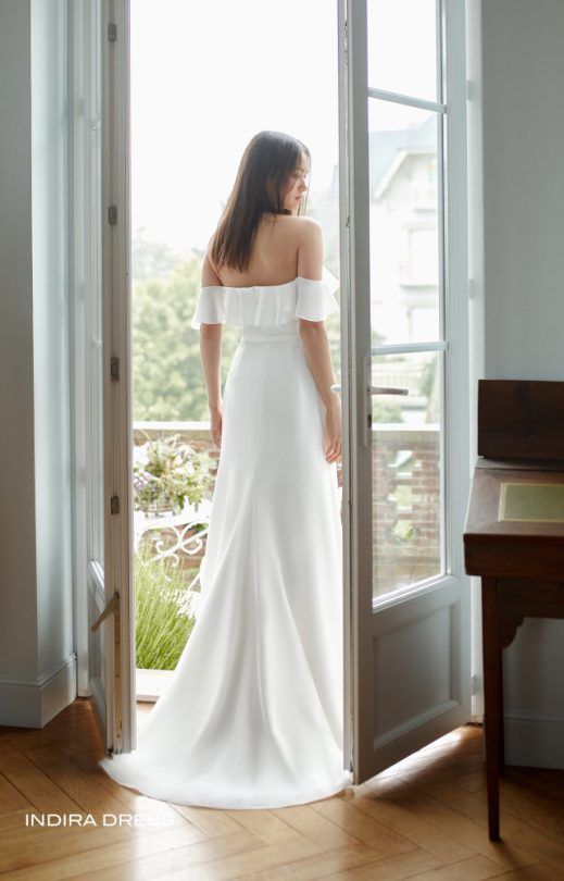 Eine Frau in einem weißen Kleid steht vor einem Fenster.