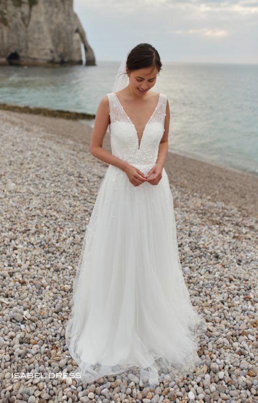 Eine Frau in einem Brautkleid steht an einem felsigen Strand in der Nähe des Meeres.