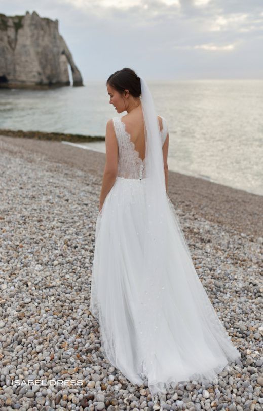 Eine Frau in einem Brautkleid steht an einem felsigen Strand in der Nähe des Meeres.