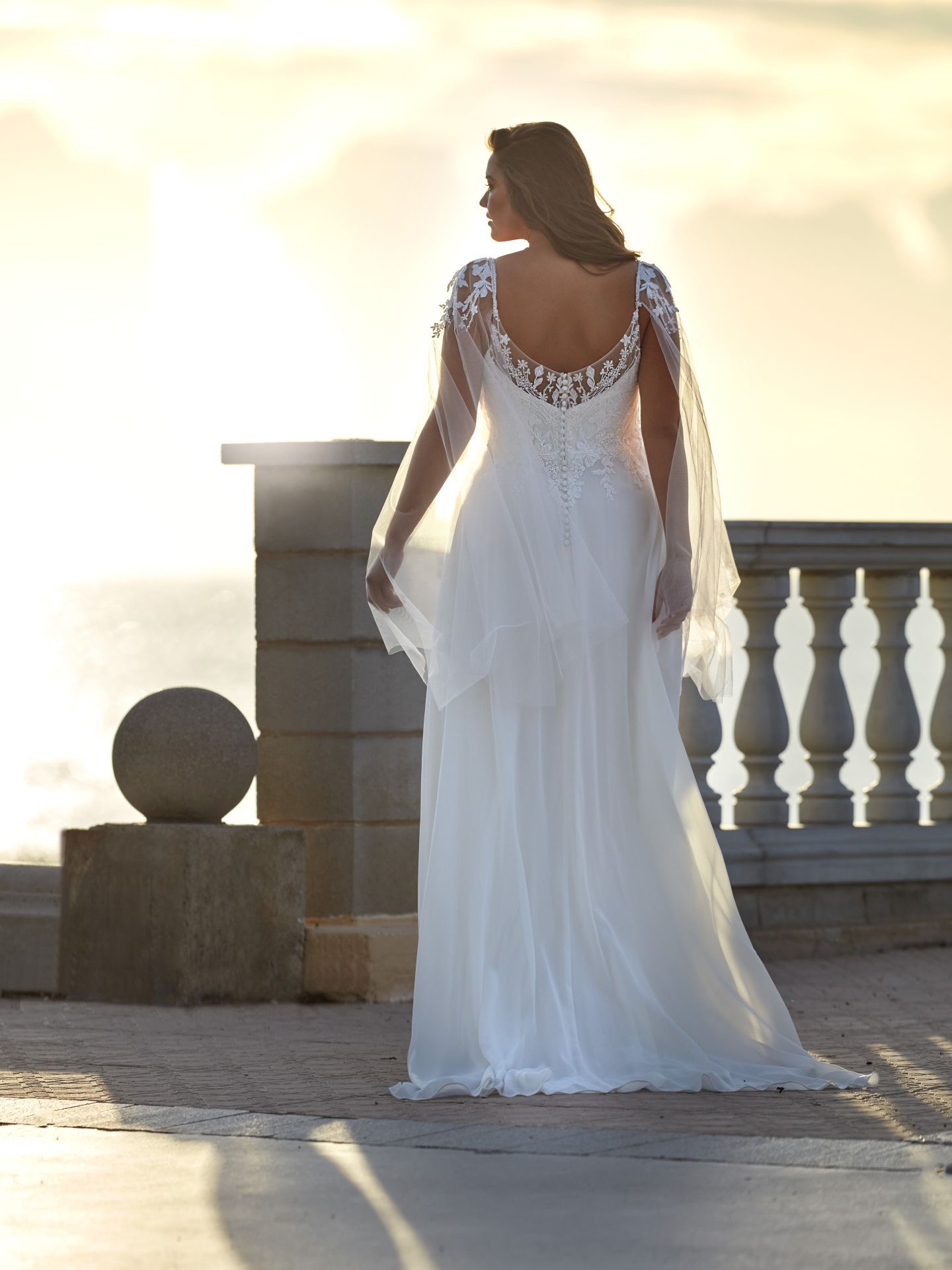 Eine Frau in einem weißen Kleid steht auf einem Balkon mit Blick auf den Ozean