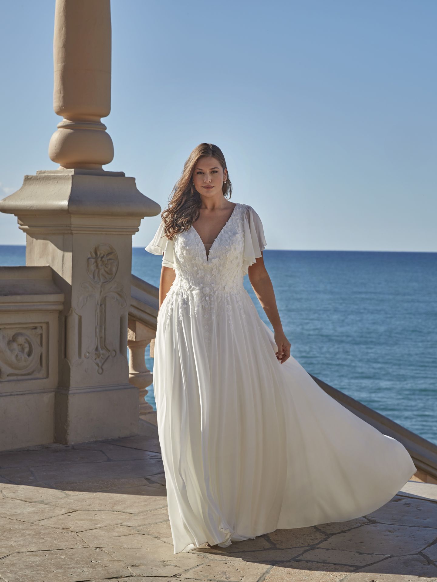 Eine Frau in einem weißen Brautkleid steht vor dem Meer.
