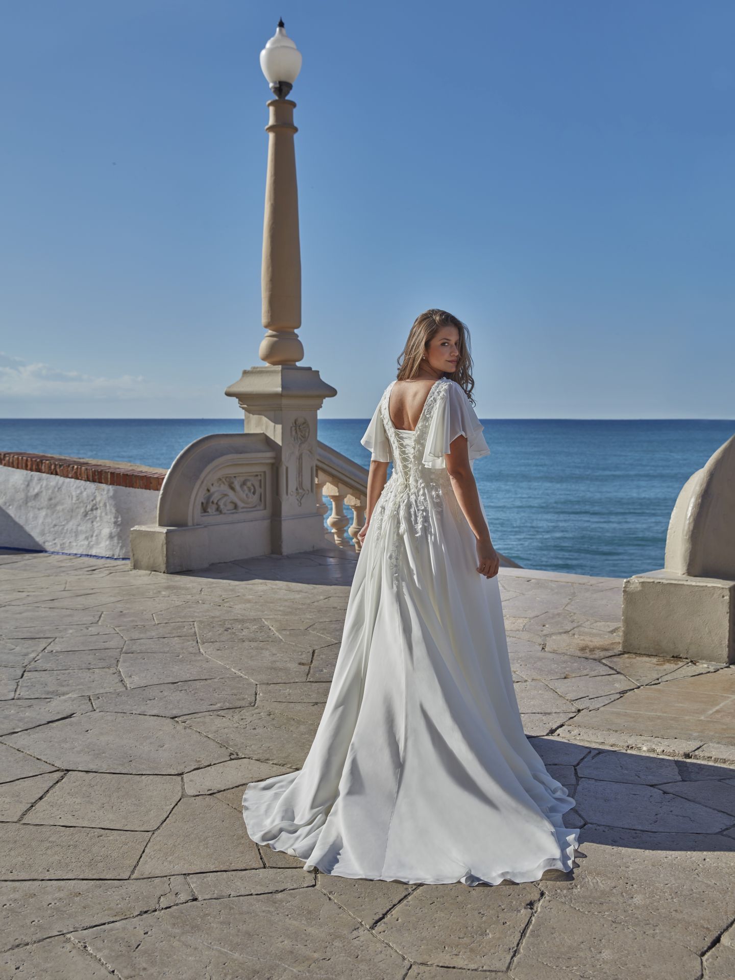 Eine Frau in einem weißen Kleid steht vor dem Meer.